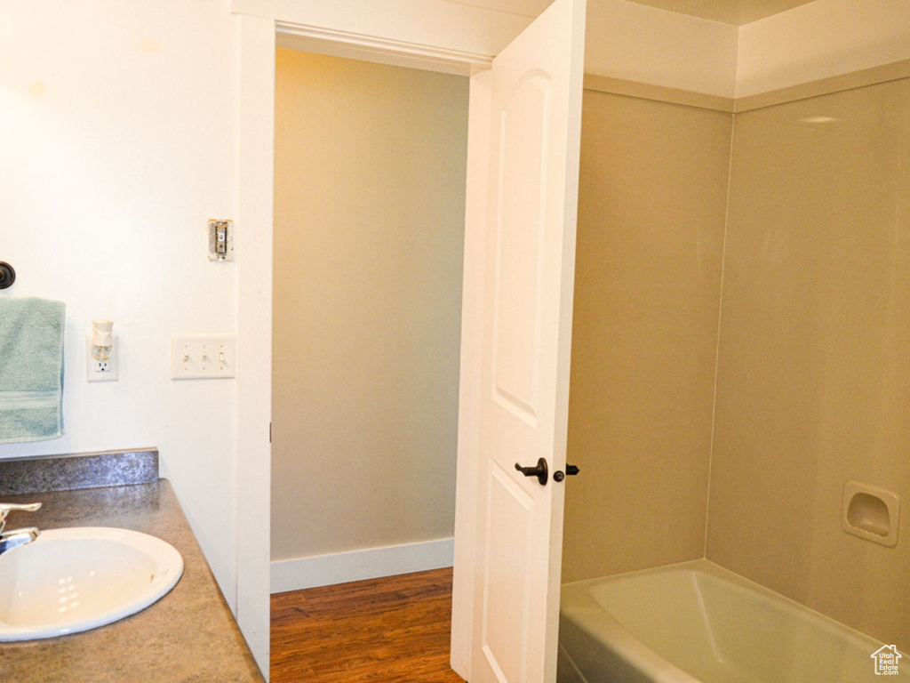 Full bath with a sink, washtub / shower combination, wood finished floors, and baseboards