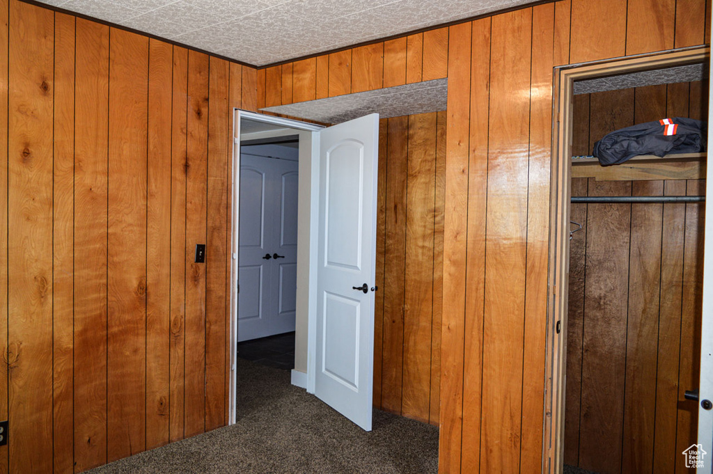Unfurnished bedroom featuring a closet, dark carpet, and wood walls
