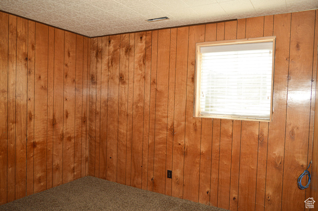 Empty room featuring wooden walls, carpet flooring, and visible vents
