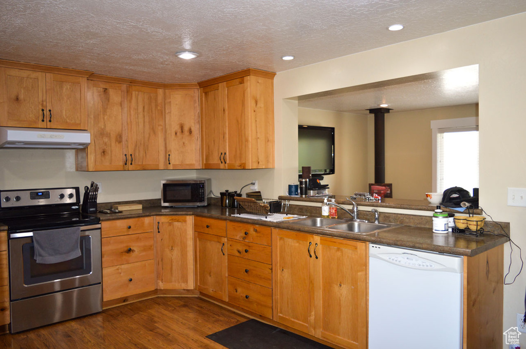 Kitchen featuring dark wood-style floors, a sink, stainless steel appliances, under cabinet range hood, and a textured ceiling