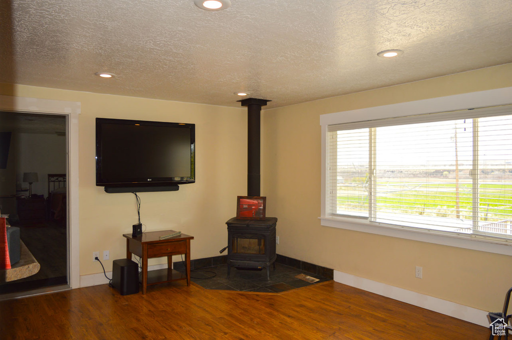 Living room featuring a wood stove, a textured ceiling, wood finished floors, and baseboards