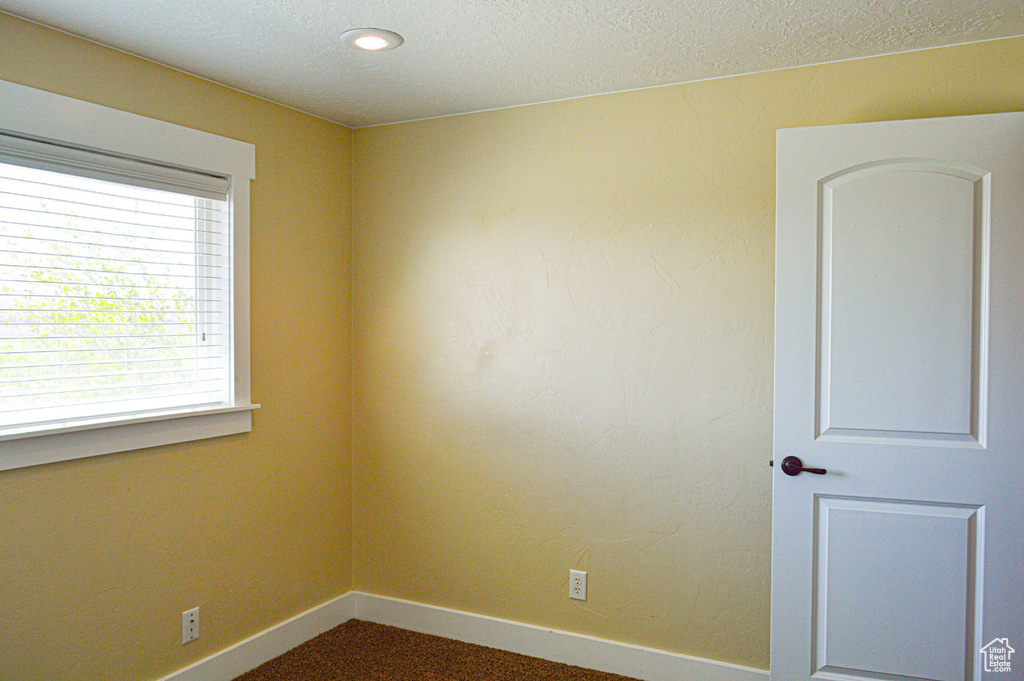 Unfurnished room featuring a textured ceiling, dark colored carpet, and baseboards