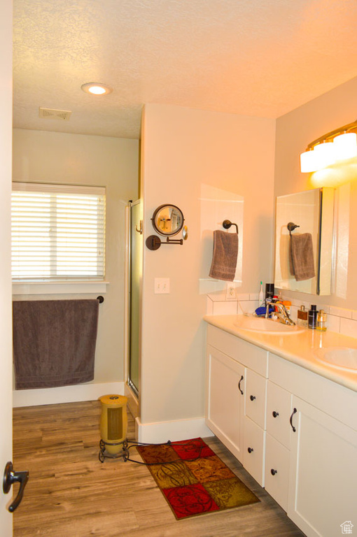 Full bath with double vanity, a shower with shower door, wood finished floors, and a sink