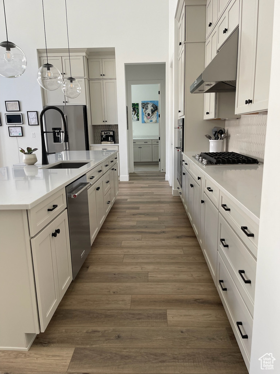 Kitchen featuring decorative backsplash, appliances with stainless steel finishes, light countertops, under cabinet range hood, and dark wood finished floors