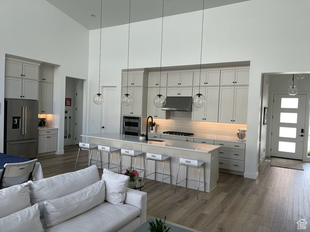Kitchen featuring high end fridge, under cabinet range hood, a sink, open floor plan, and a towering ceiling