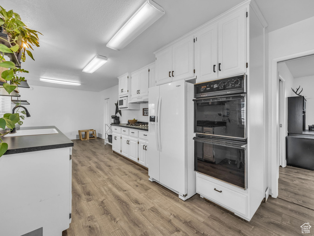 Kitchen featuring dobule oven black, dark countertops, white refrigerator with ice dispenser, a sink, and white cabinetry