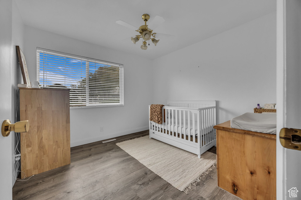 Bedroom with a ceiling fan, a crib, and wood finished floors