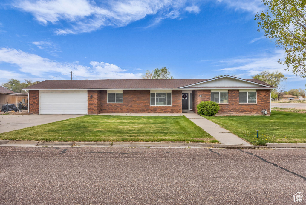 Ranch-style house featuring a garage, concrete driveway, a front lawn, and brick siding