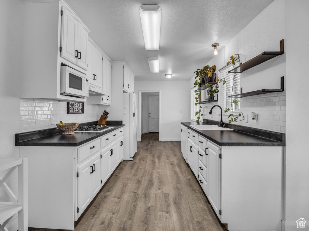 Kitchen featuring a sink, dark countertops, open shelves, and white appliances