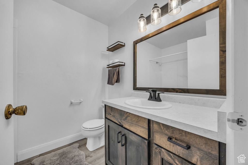 Full bath featuring toilet, baseboards, wood finished floors, and vanity