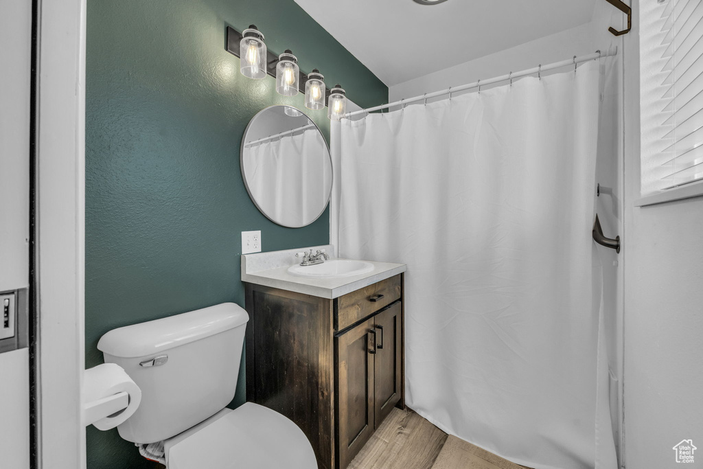 Bathroom featuring toilet, a textured wall, wood finished floors, and vanity