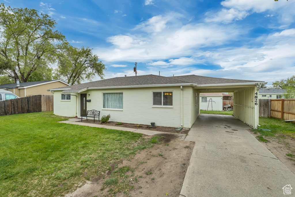 Back of house featuring a shingled roof, a lawn, driveway, a carport, and fence