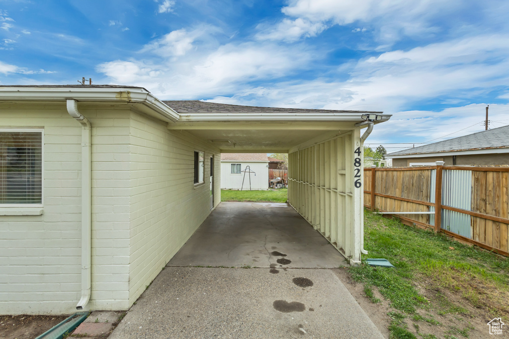 View of side of home featuring a carport, a shingled roof, and fence