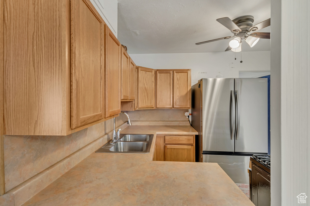 Kitchen featuring a ceiling fan, a sink, light countertops, and freestanding refrigerator