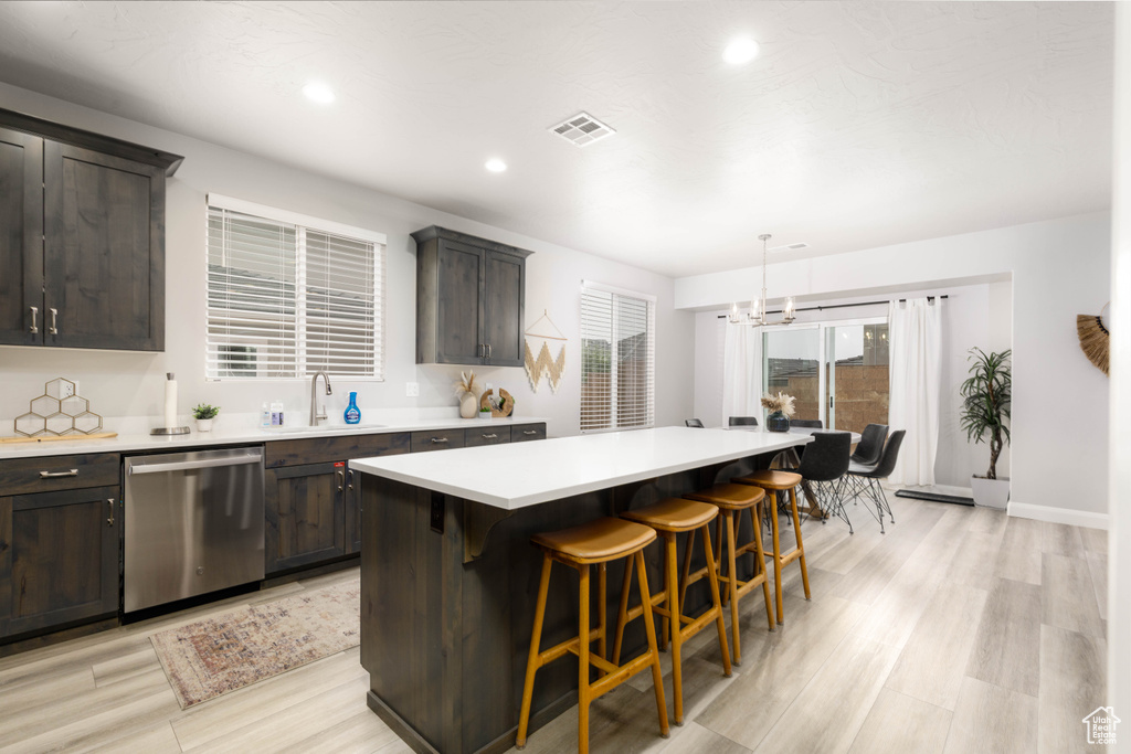 Kitchen featuring stainless steel dishwasher, a sink, dark brown cabinets, light countertops, and recessed lighting