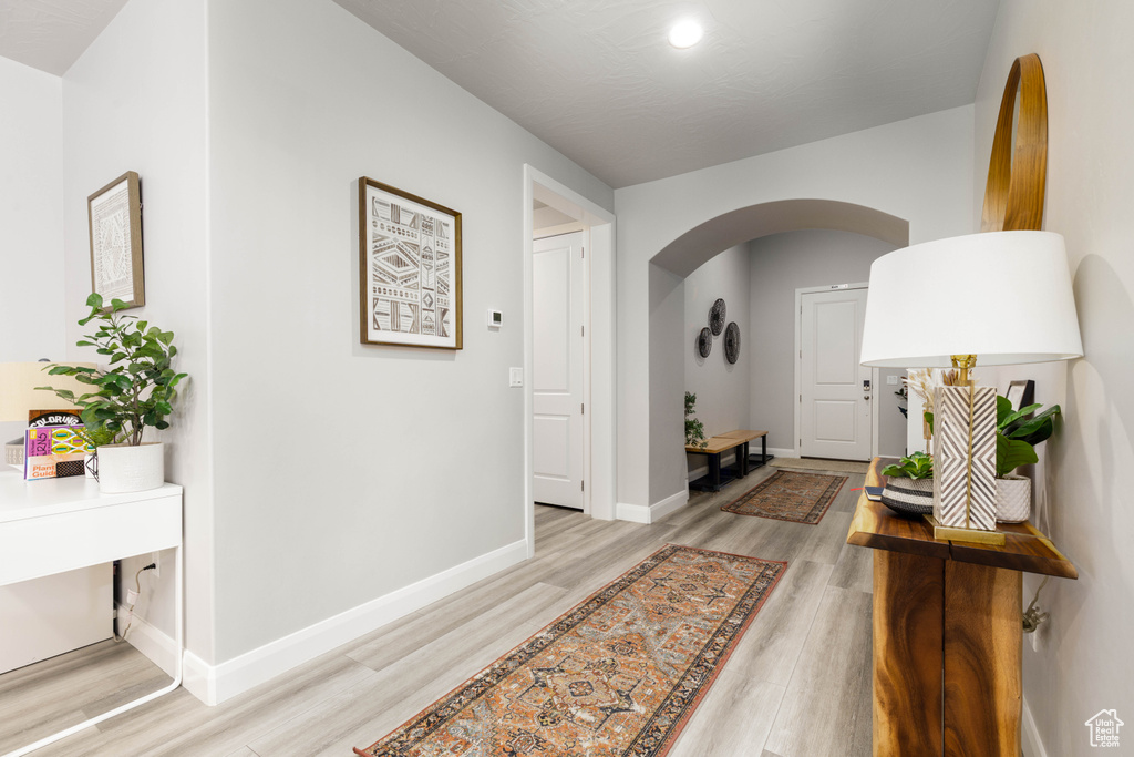 Hall with arched walkways, light wood-style flooring, baseboards, and recessed lighting
