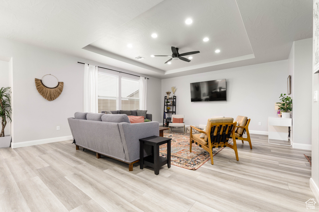 Living area featuring a tray ceiling, recessed lighting, a ceiling fan, light wood-type flooring, and baseboards