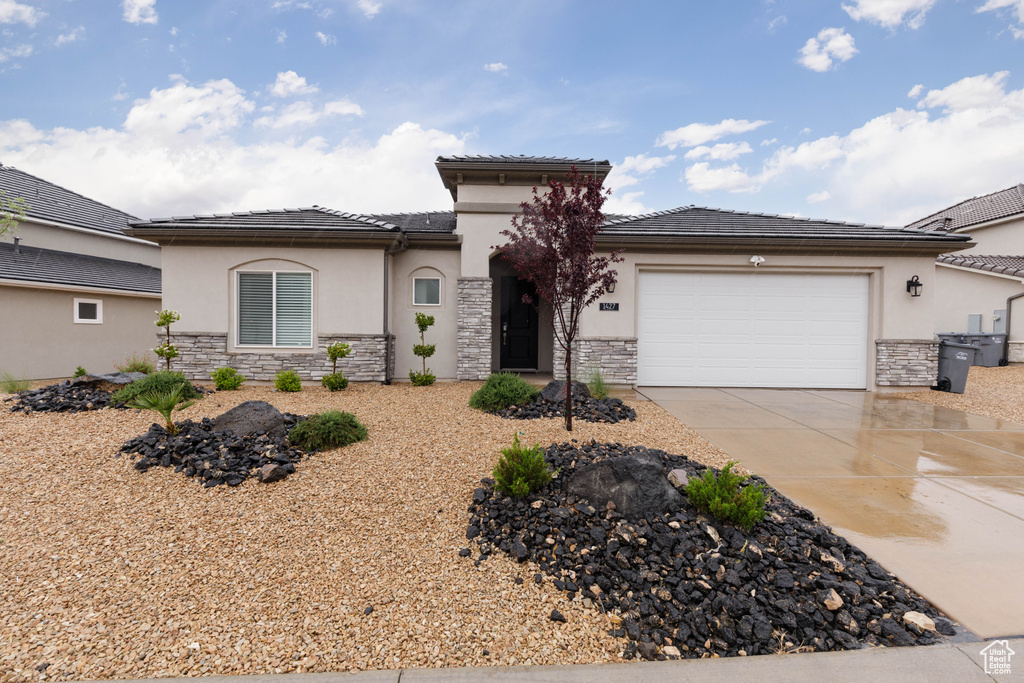 View of front of property featuring stone siding, stucco siding, an attached garage, and driveway