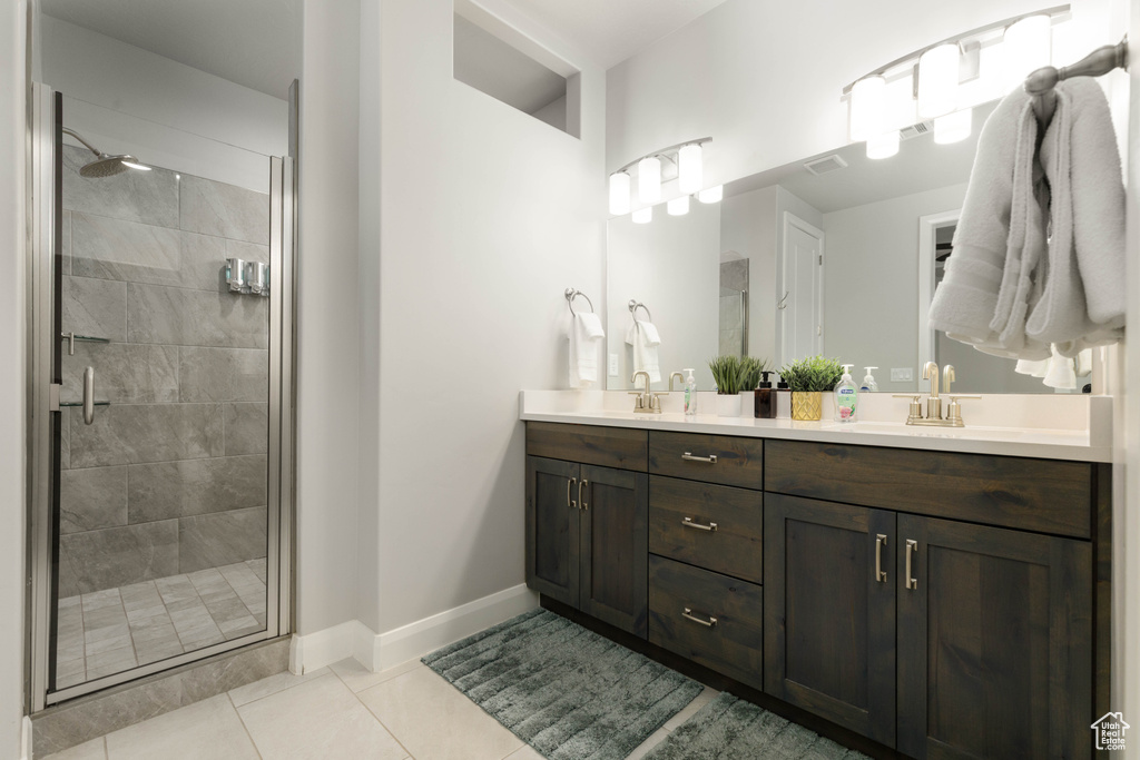 Bathroom featuring a shower stall, tile patterned floors, double vanity, and baseboards