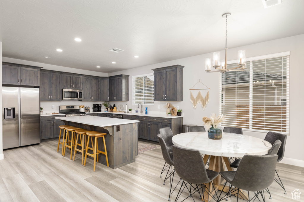 Kitchen featuring stainless steel appliances, dark brown cabinets, a chandelier, light countertops, and a center island