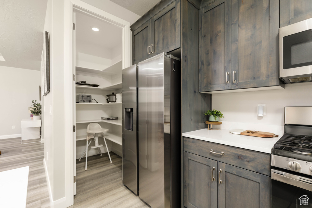 Kitchen featuring stainless steel appliances, light wood finished floors, light countertops, dark brown cabinetry, and recessed lighting