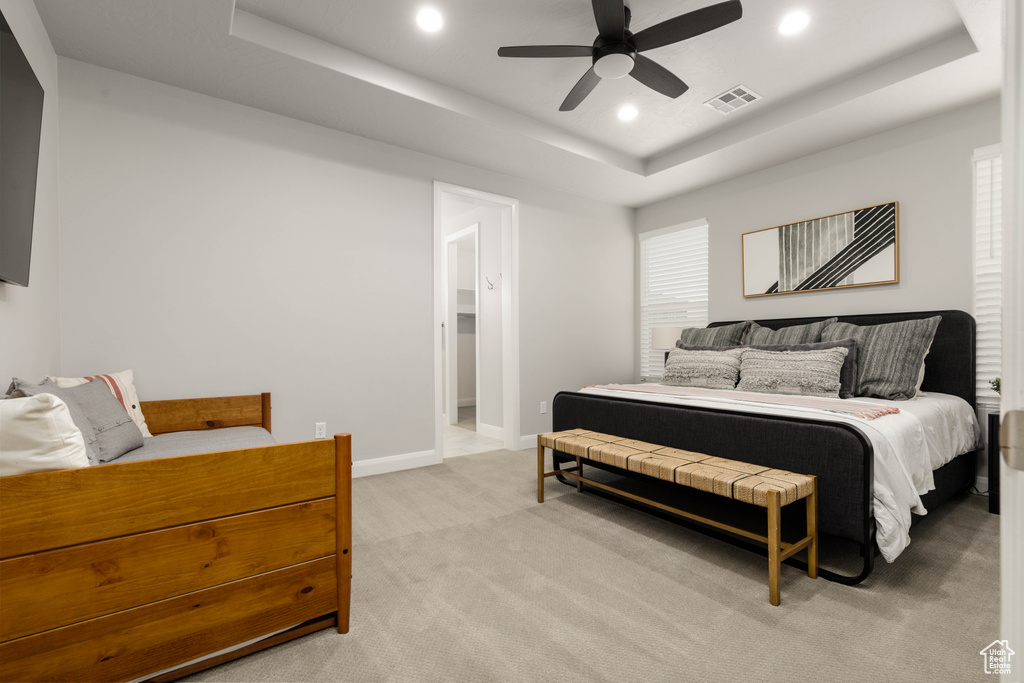 Bedroom with a raised ceiling, light colored carpet, recessed lighting, baseboards, and a ceiling fan