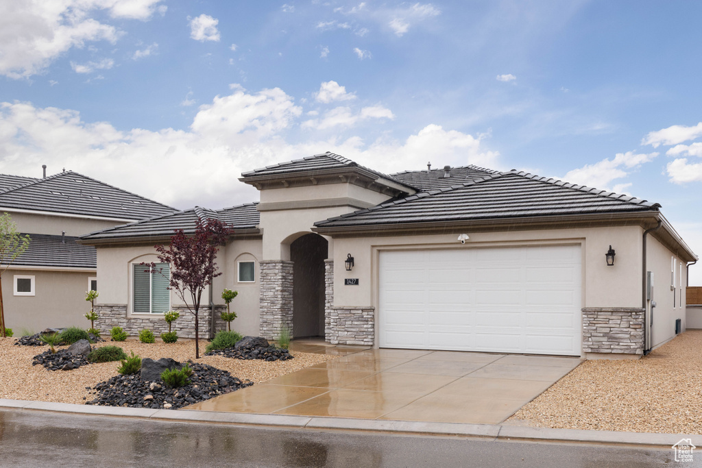 View of front of house with stone siding, stucco siding, driveway, an attached garage, and a tiled roof