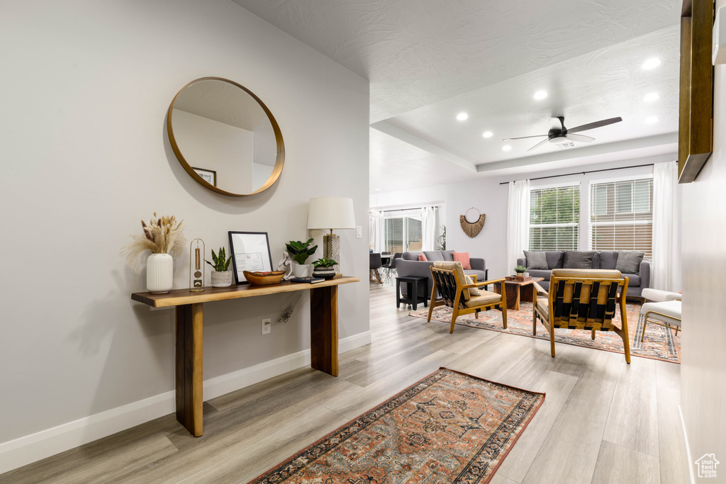 Interior space with light wood-style flooring, recessed lighting, a tray ceiling, a ceiling fan, and baseboards