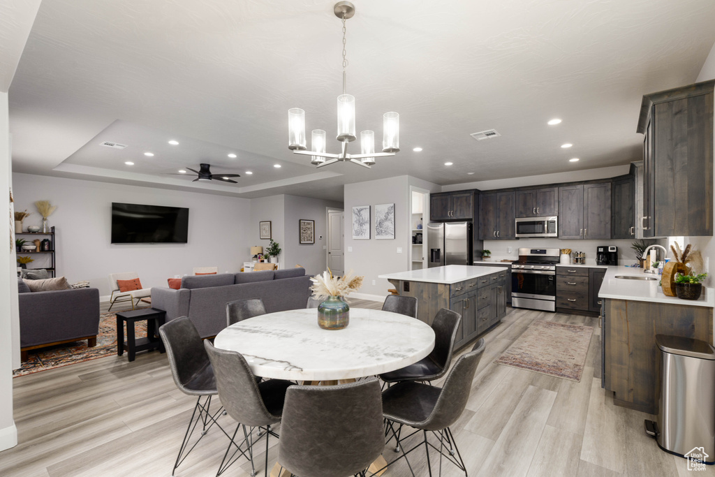 Dining room featuring a chandelier, a ceiling fan, light wood-style floors, recessed lighting, and a tray ceiling