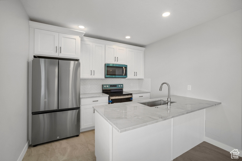 Kitchen with white cabinetry, appliances with stainless steel finishes, a sink, baseboards, and a peninsula