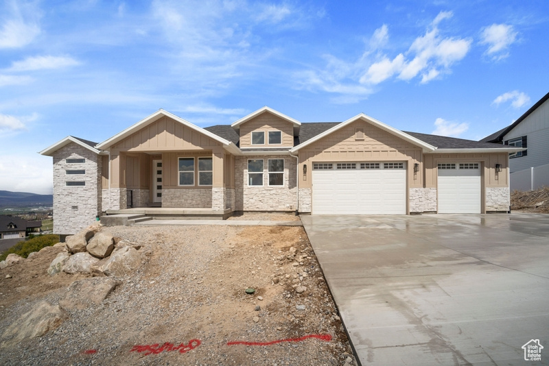 View of front of house featuring covered porch, driveway, an attached garage, and stone siding