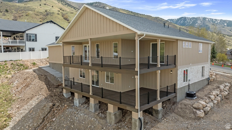 Back of house with a mountain view, roof with shingles, central AC unit, and a balcony