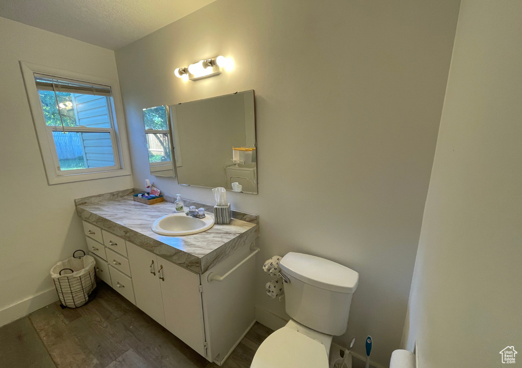 Half bathroom with wood finished floors, toilet, vanity, baseboards, and a textured ceiling