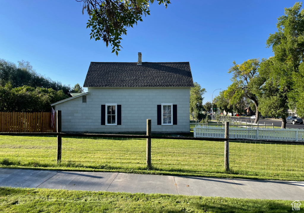 View of property exterior featuring a chimney, fence, roof with shingles, and a lawn