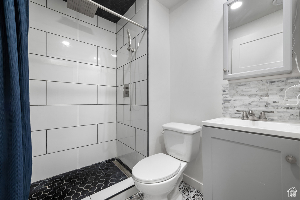 Bathroom with tasteful backsplash, toilet, vanity, and tiled shower