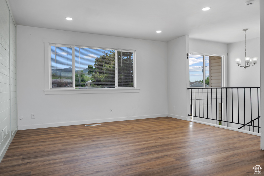 Unfurnished room with healthy amount of natural light, wood finished floors, baseboards, a chandelier, and recessed lighting