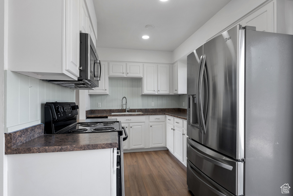 Kitchen with stainless steel appliances, a sink, dark countertops, white cabinets, and dark wood-style floors