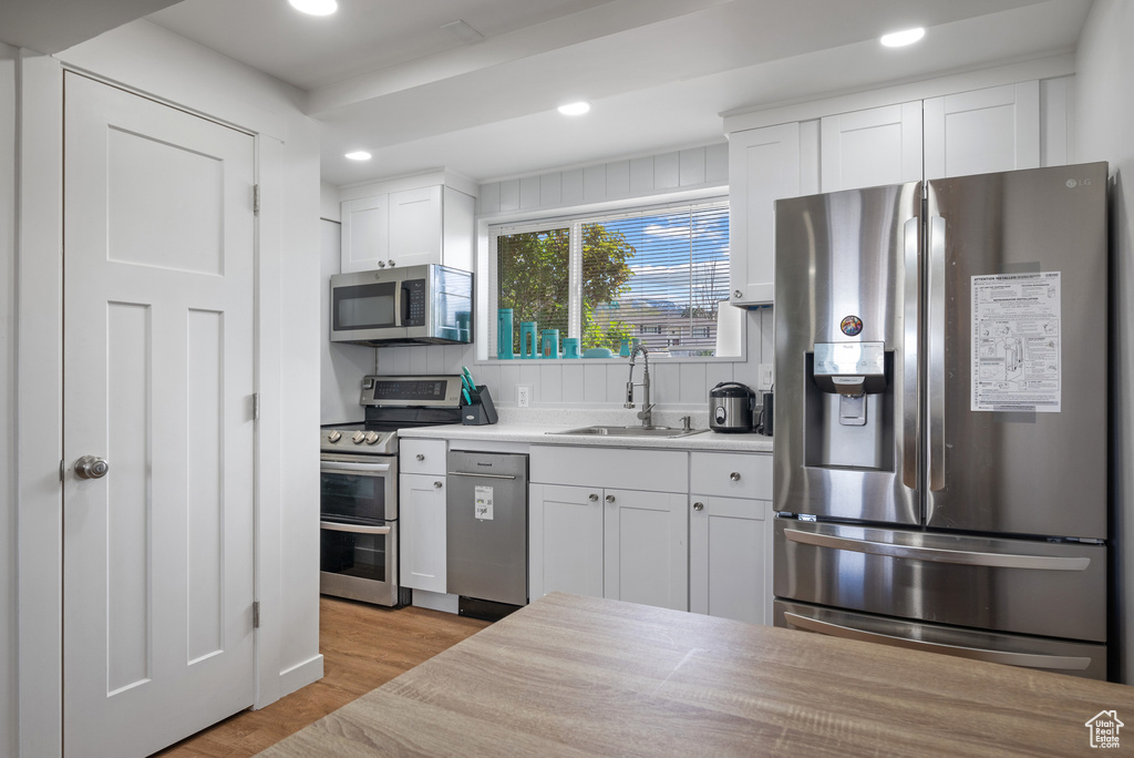 Kitchen with appliances with stainless steel finishes, a sink, light wood finished floors, white cabinetry, and recessed lighting