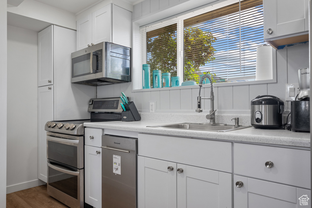Kitchen with stainless steel appliances, a sink, light countertops, wood finished floors, and white cabinets