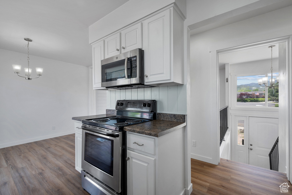 Kitchen with appliances with stainless steel finishes, a chandelier, dark countertops, dark wood-style floors, and white cabinets
