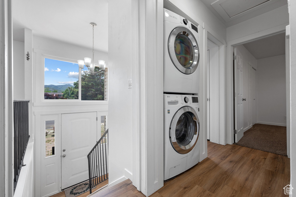Laundry area featuring stacked washing machine and dryer, wood finished floors, and a chandelier