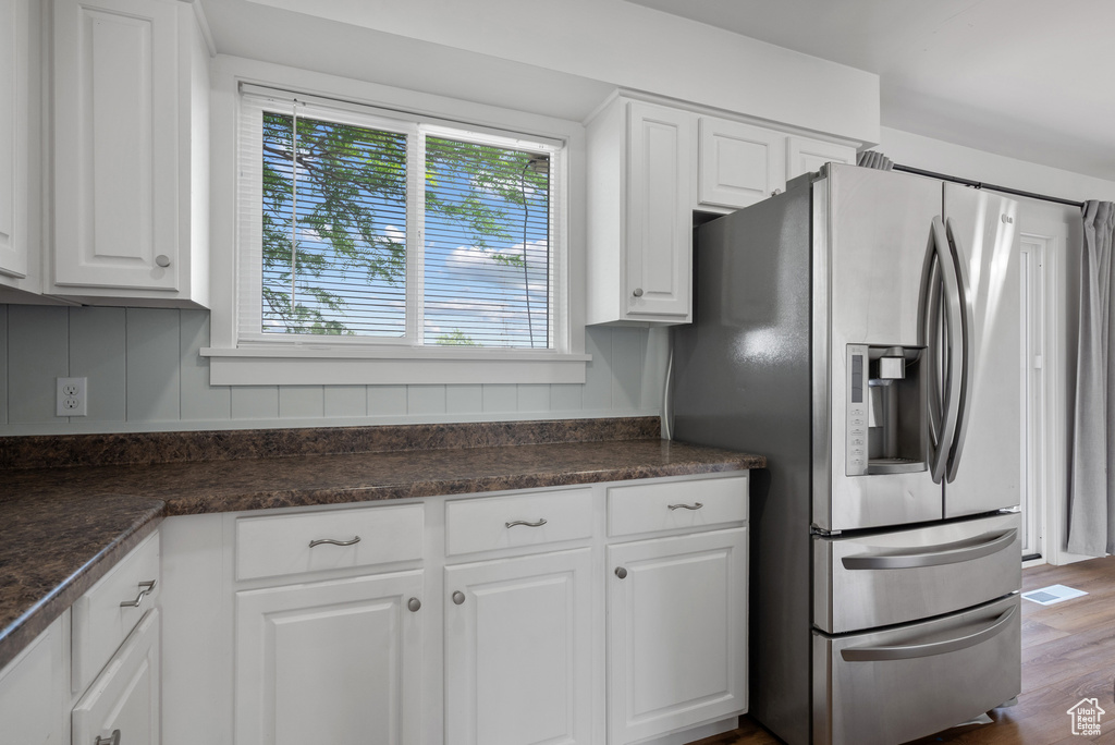 Kitchen featuring stainless steel fridge with ice dispenser, dark countertops, white cabinets, and wood finished floors