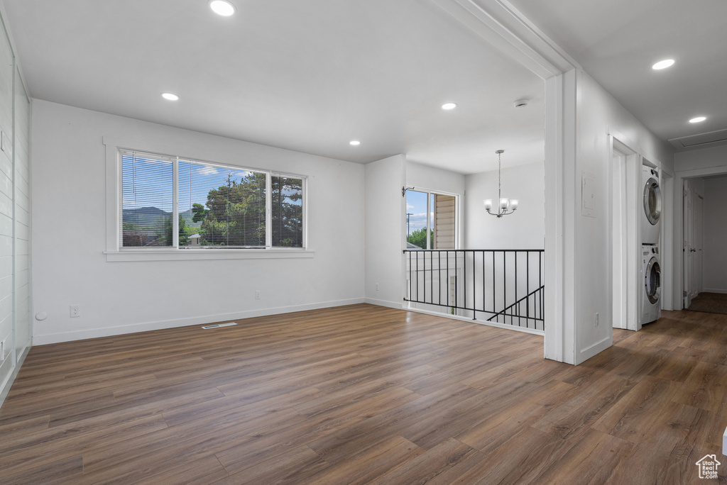 Empty room featuring stacked washer and clothes dryer, wood finished floors, recessed lighting, baseboards, and a chandelier