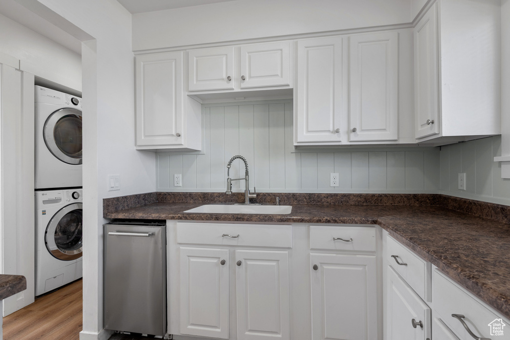 Kitchen featuring stacked washer / dryer, a sink, white cabinetry, and light wood-style flooring