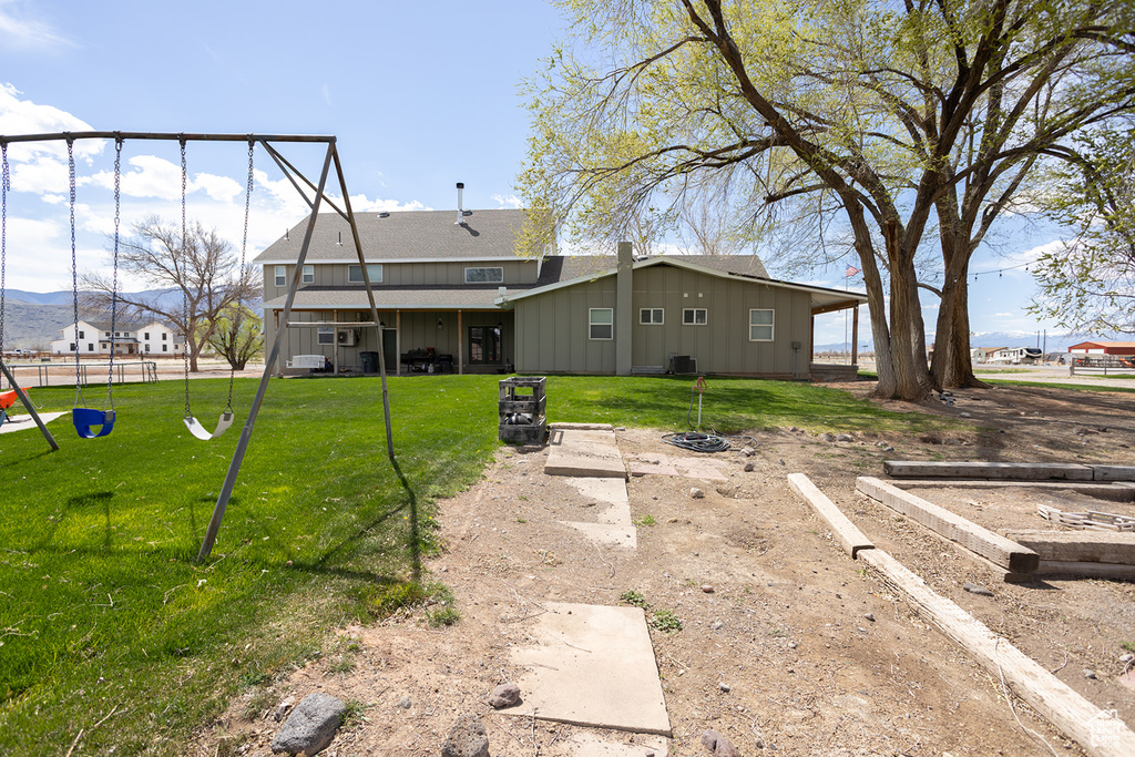 Back of house featuring a lawn, board and batten siding, central AC unit, and a playground