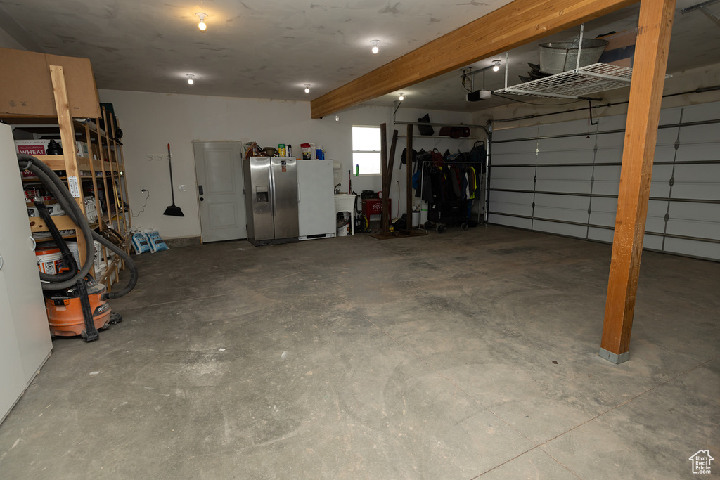 Garage with a garage door opener, freestanding refrigerator, and stainless steel fridge with ice dispenser
