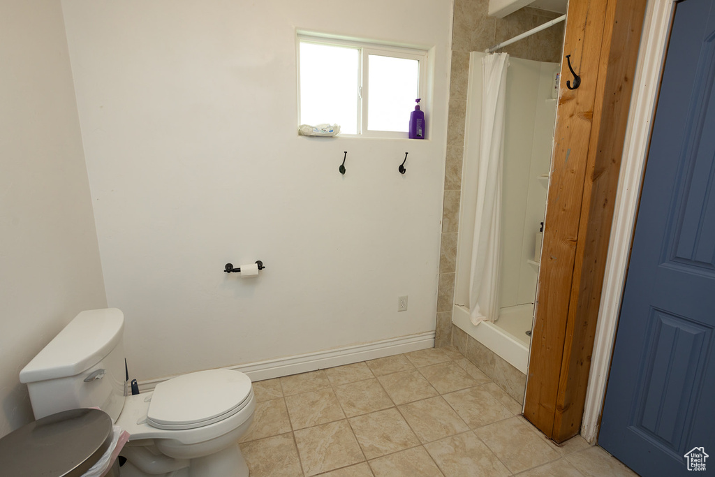 Bathroom featuring curtained shower, toilet, and tile patterned flooring