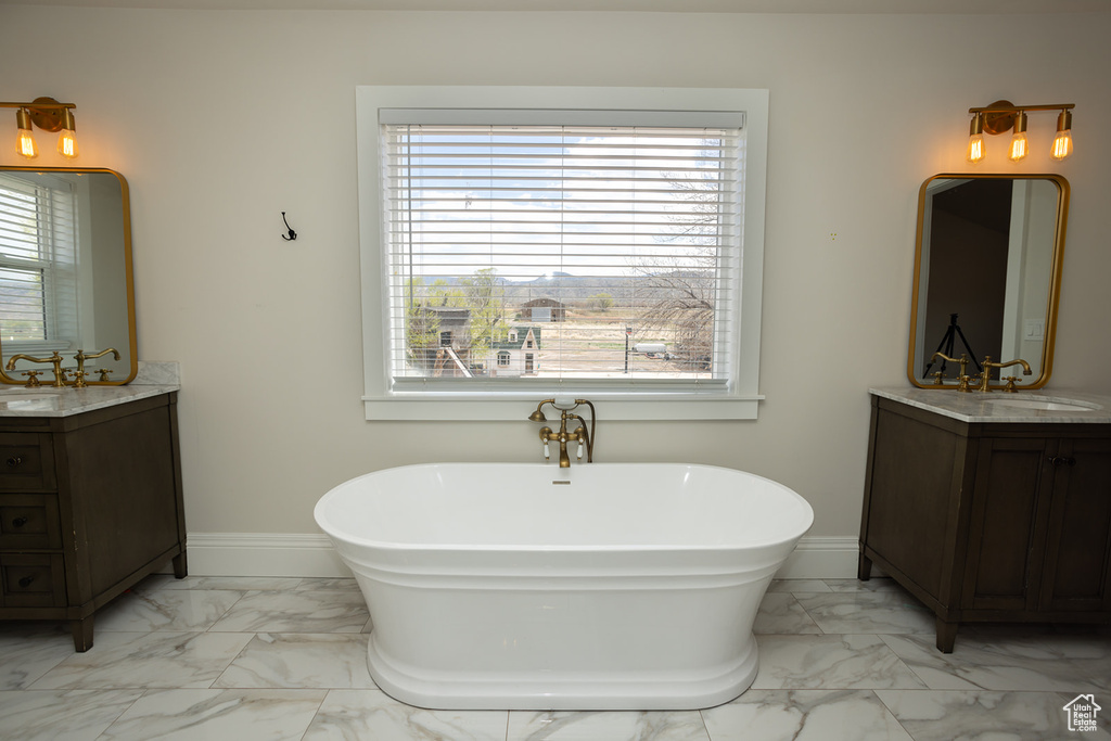 Bathroom with a sink, a freestanding tub, marble finish floor, two vanities, and baseboards