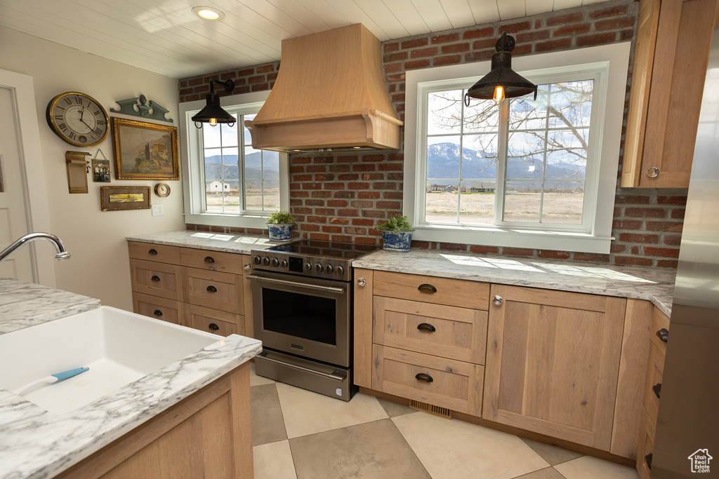Kitchen with stainless steel electric range oven, custom range hood, and plenty of natural light
