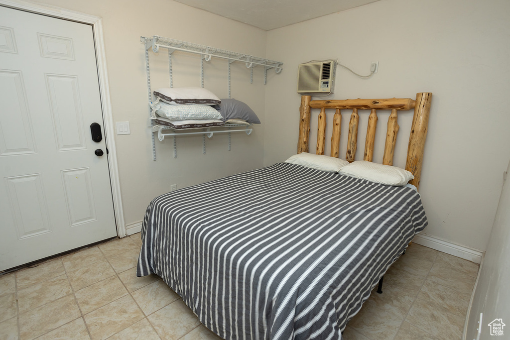 Bedroom with light tile patterned floors, an AC wall unit, and baseboards